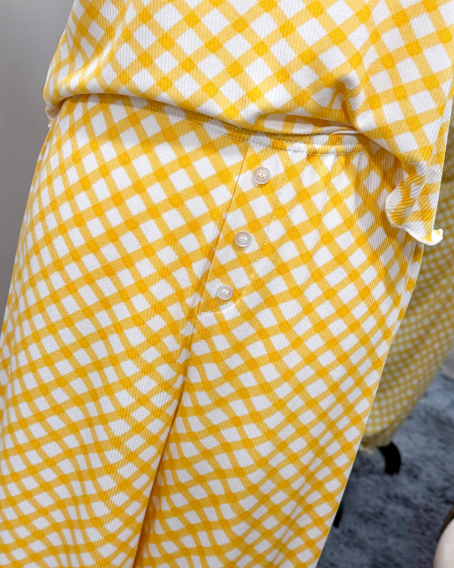 Yellow and white checkered pajama pants with decorative button fly on a neutral background