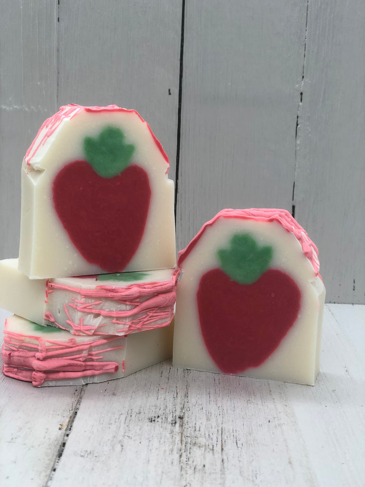Strawberry scented white soap bars with a red strawberry with a green stem in the middle and sprinkled with pinkish red swirl on the top