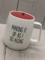 A white mug with text that reads "MAKING IT UP AS I GO ALONG". The inside is pink.