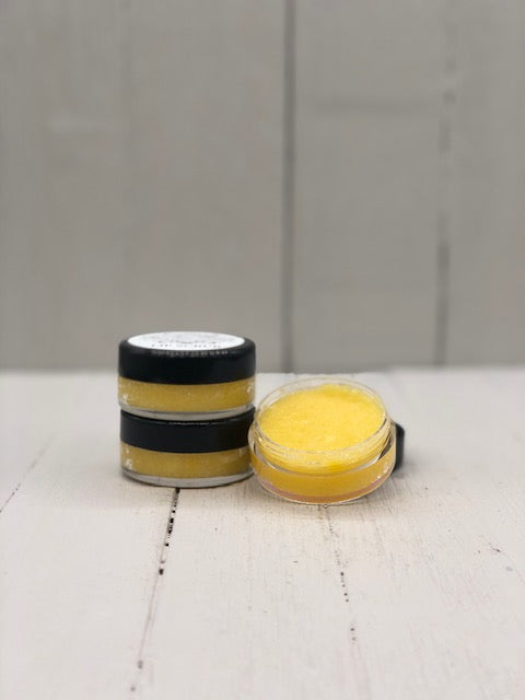Yellow lip scrub in a small clear pot with a black lid.