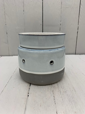 A circular ceramic wax warmer. It is light gray with a band of dark gray on the bottom. There are two holes where light can shine through.